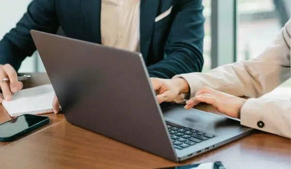 Two business people at a desk consulting behind a laptop.