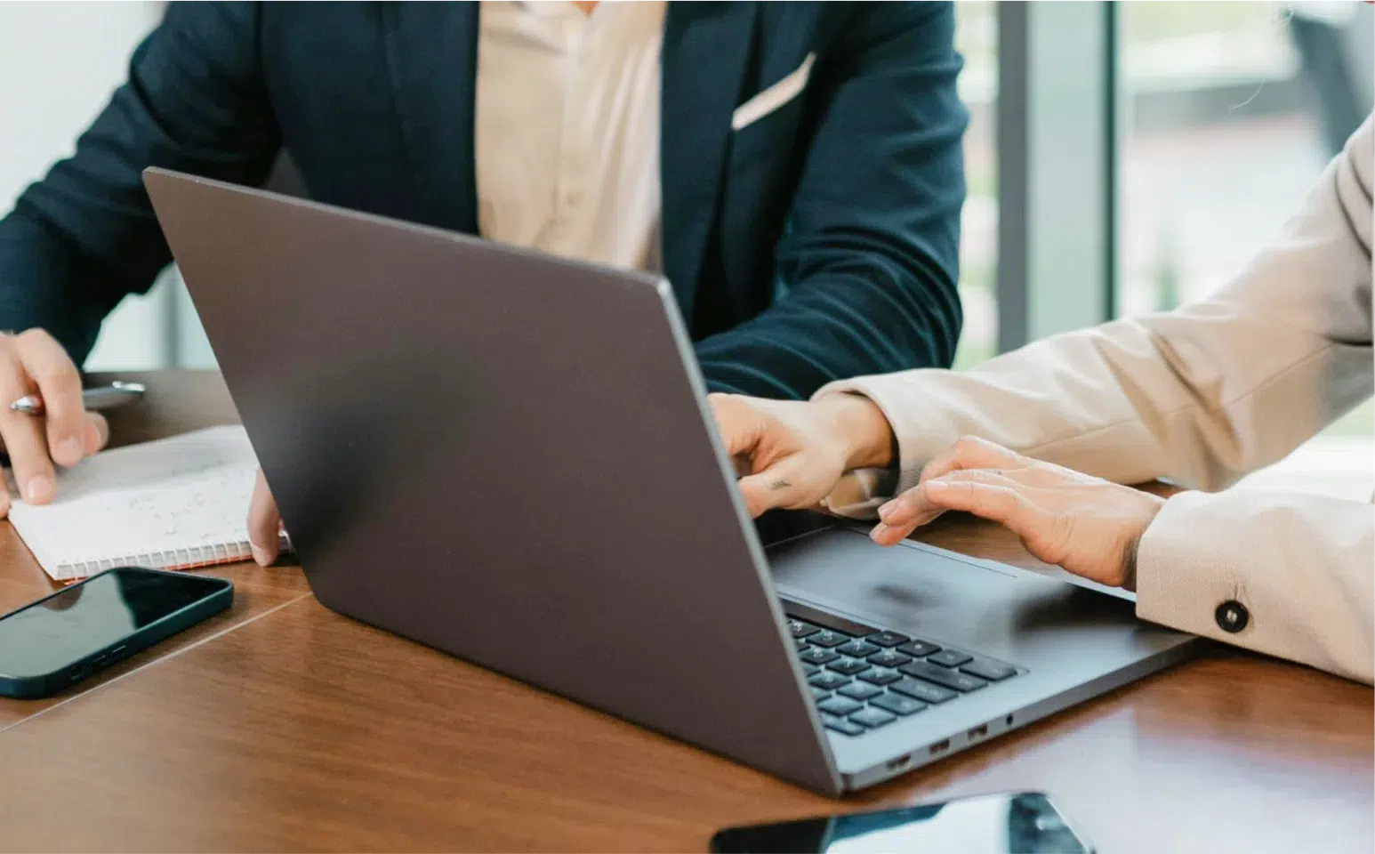 Two business people at a desk consulting behind a laptop.