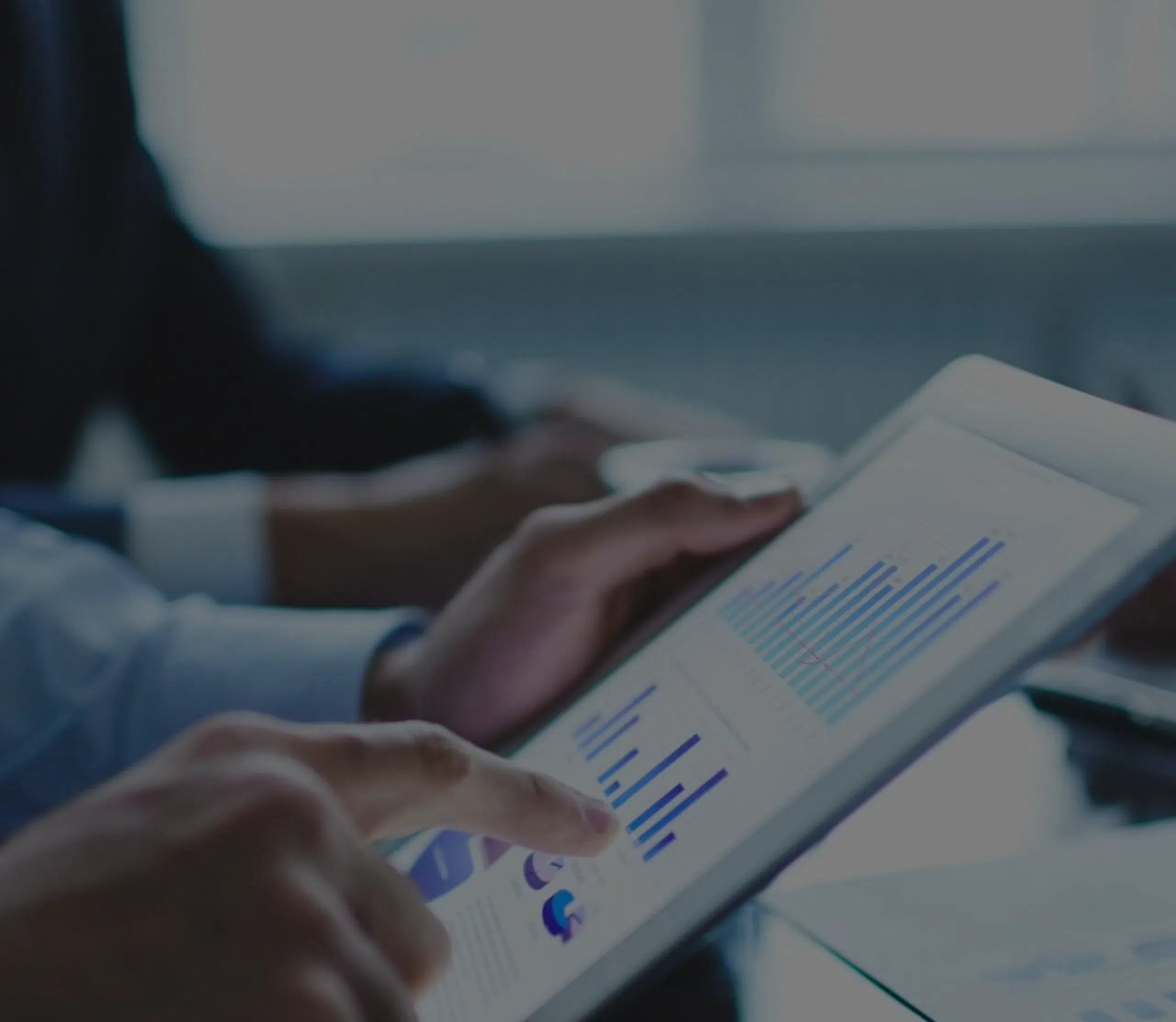 Close-up of an executive's hands, one holding a tablet displaying graphs and KPIs.