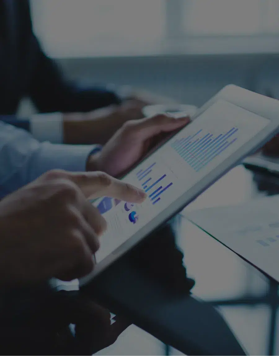 Close-up of an executive's hands, one holding a tablet displaying graphs and KPIs.