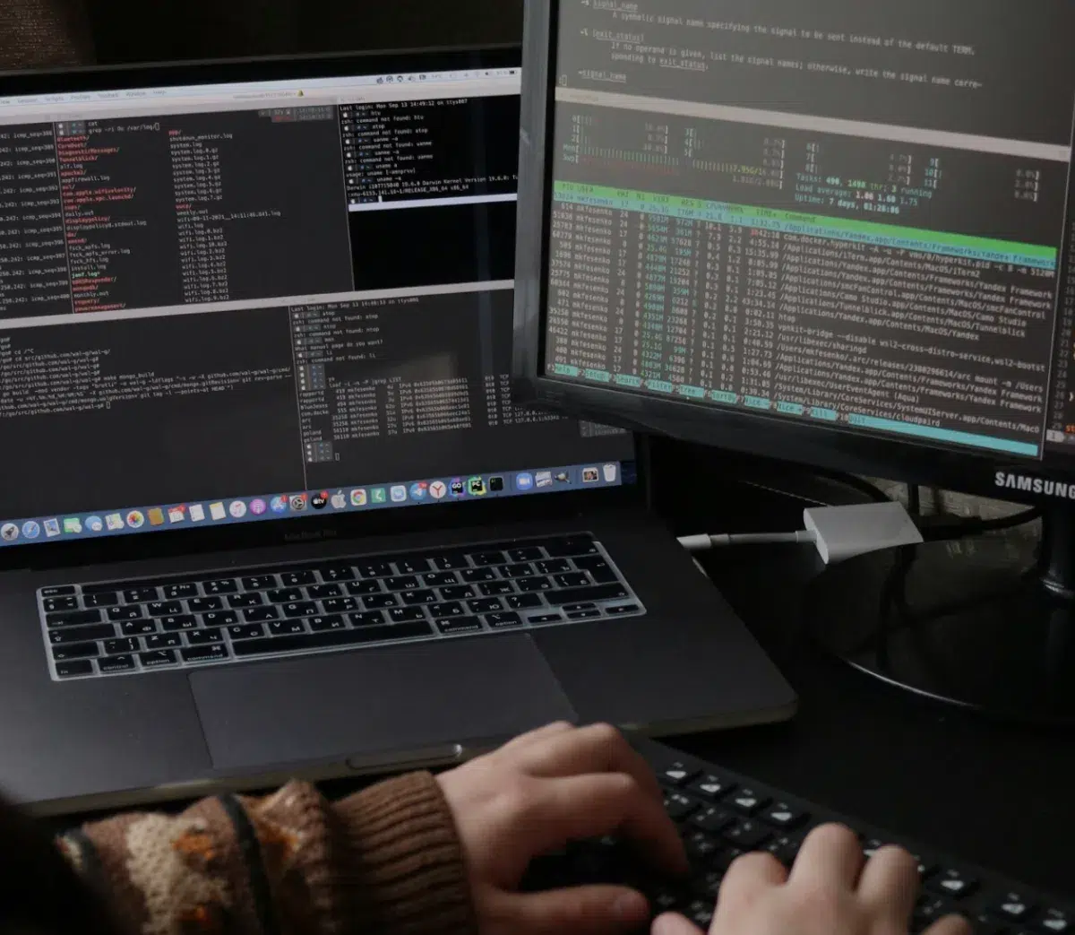 Hands of a software developer typing on a keyboard at a dual-monitor computer setup