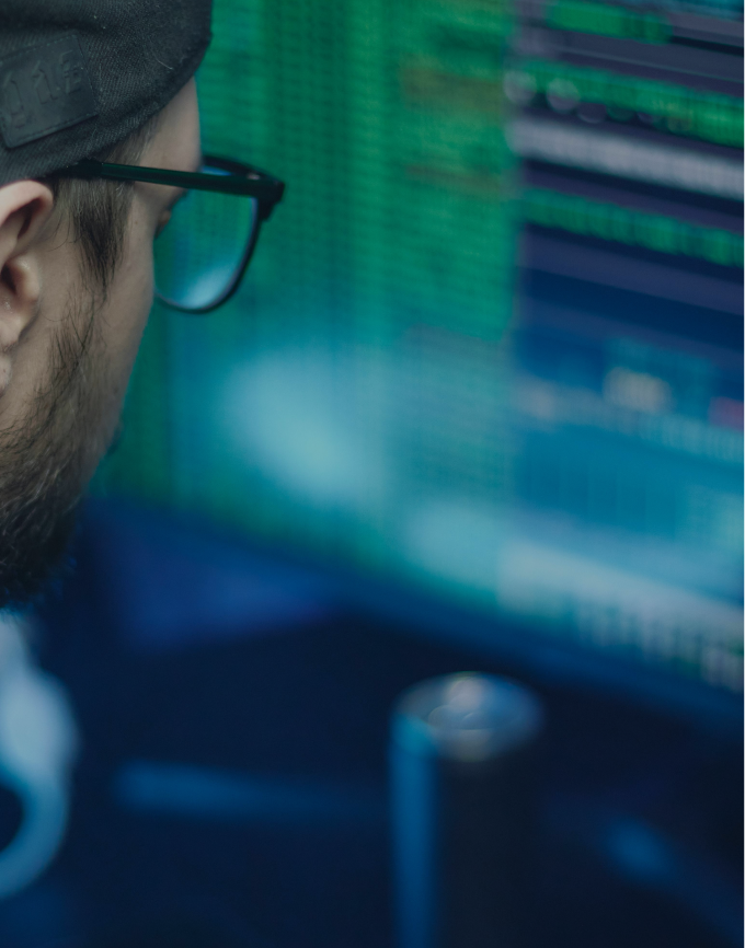 Close-up of a developer in front of a computer screen displaying code in the background.